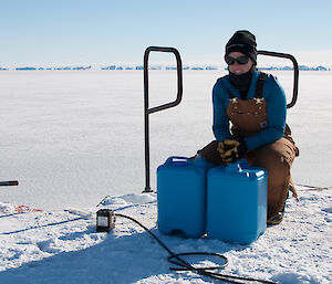 Expeditioner kneeling alongside blue water barrels at the wharf