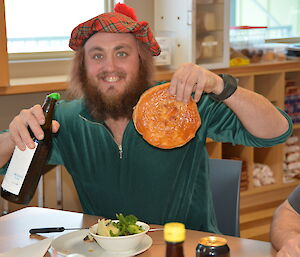 Expeditioner dressed in green wearing a tartan hat holding a guinness pie