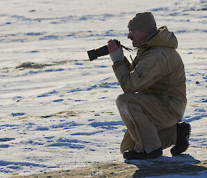 Exeditioner kneeling on the snow taking a photo