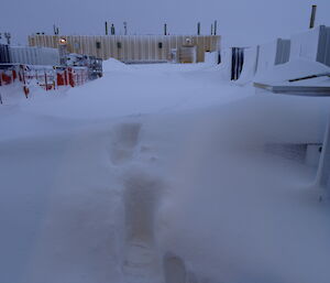 Deep footprints in the snow with green store in background