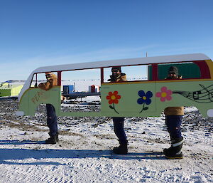 Three expeditioners holding a timber frame painted in the shape of a kombi van