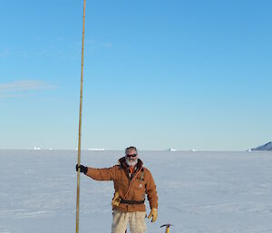 Expeditioner standing alongside an upright cane in the sea ice