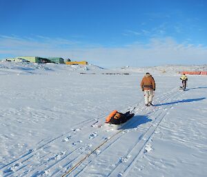 Two expeditioners walking back to station on the sea ice towing sleds