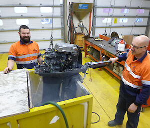 Two expeditioners working on an outboard motor in the workshop