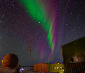 Green and red aurora over station buildings