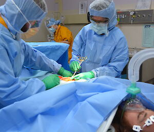 Patient under surgical sheets surrounded by medical team