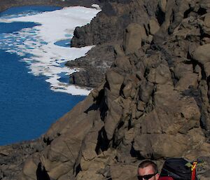 Expeditioner standing on a rock ledge with a lake in the background