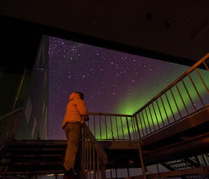 Expeditioner outside the living quarters with stunning aurora