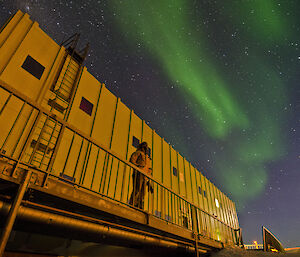 Expeditioner standing outside building with aurora overhead