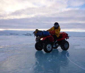 Expeditioner on quad bike looking down into clear sea ice