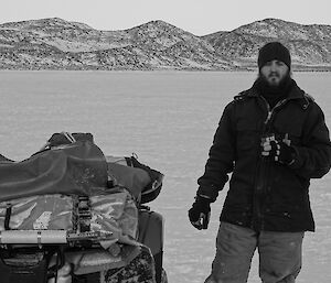 Black and white photo of expeditioner standing next to quad bike drinking tea