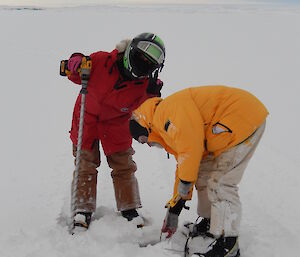 Expeditioners leaning over drilled hole in ice to measure depth