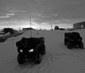 Two quad bikes loaded with gear parked outside buildings