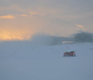 Red Hägglunds on the beach with low visibility and blowing snow, station in the background