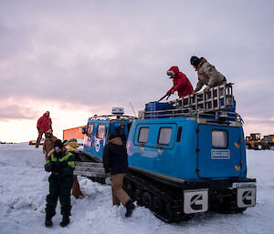 Expeditioners taking gear down from the roof of the Hägglunds