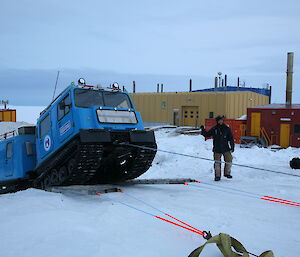 An expeditioner guides a Hägglunds oversnow vehicle that is being pulled by ropes in a recovery training exercise