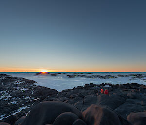 Two expeditioners in the distance sitting on rocks, one proposing marriage to the other