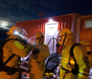 Three expeditioners dressed in fire fighting gear outside a building