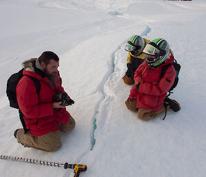 Three expeditioners leaning over a tide crack in the sea ice