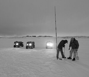 Black and white image of two expeditioners drilling hole in sea ice