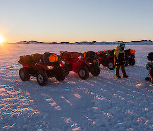 Three people standing next to quads drilling sea ice