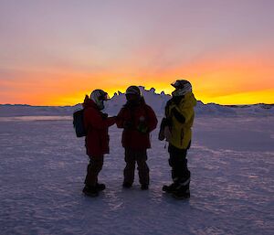 Three expeditioners standing on sea ice stunning sunrise in the background