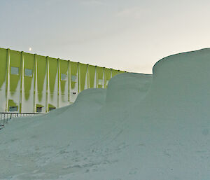 A large mountain of snow built up alongside a gree building