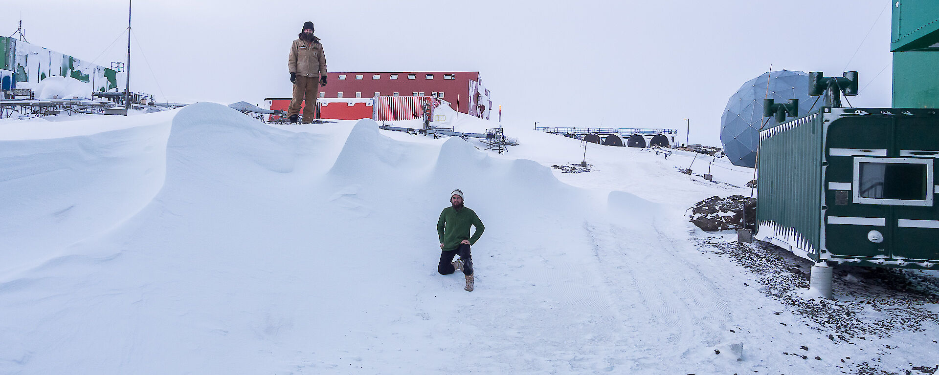 One expeditioner standing on top of the large snow drift the other at the base