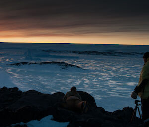 Two expeditioners standing on a rocky area watching the sun set