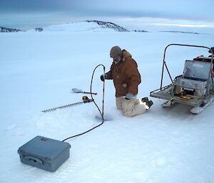 Expeditioner kneeling on sea ice installing buoy through hole in ice
