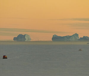 Hägglunds on sea ice driving towards small tent with orange sunset in background
