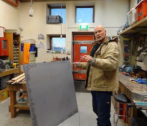 Expeditioner in workshop holding a large metal window shutter