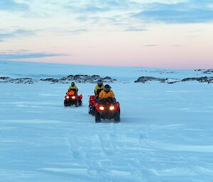 Three expeditioners riding quad bikes on the sea ice