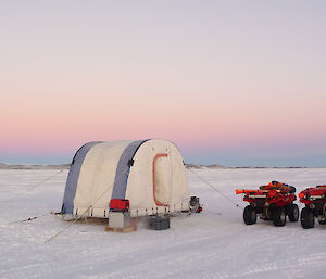 white round top tent on the sea ice with 2 quads