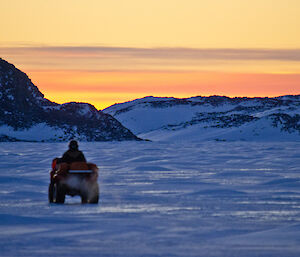 Expeditioner riding a quad on sea ice with stunning bright sunset in background