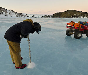 Expeditioner with electric drill drilling through smooth blue sea ice
