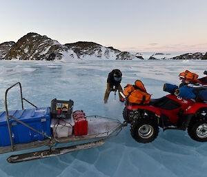 Expeditioner drilling sea ice with quad bikes in foreground