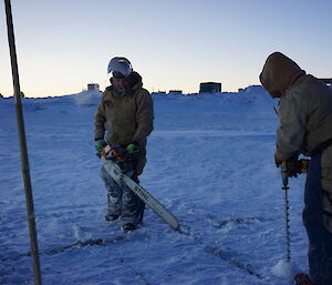 Two expeditioners one with a chainsaw marking squares in the sea ice