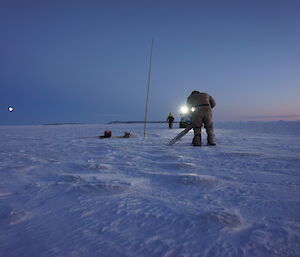 Expeditioner with chainsaw preparing to cut through the sea ice full mmon and hagglund in background