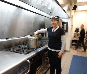 Chef standing next to large industrial gas stove stirring pot