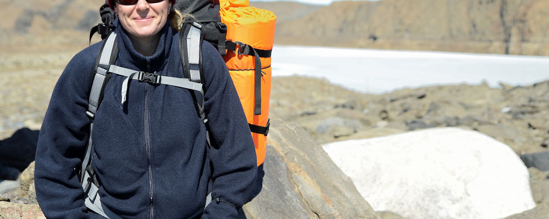 Expeditioner carrying backpack leaning against large boulder