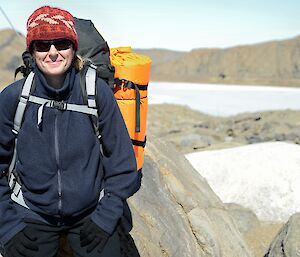 Expeditioner carrying backpack leaning against large boulder
