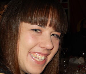 Close up photo of young, female expeditioners face framed with brown hair and fringe, grins widely