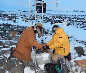 Two expeditioners kneeling alongside a small weather station