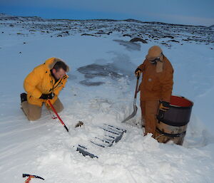 Two expeditioners with shovels clearing snow from cache