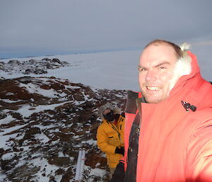 Expeditioner taking a selfie while another expeditioner is removing a small weather station