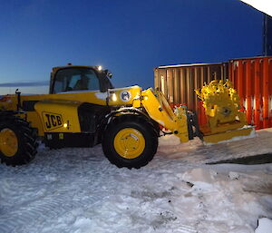 Yellow JCB with engine on it’s forks beign driven into a building