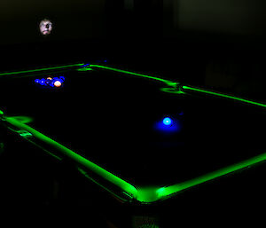 expeditioner photographs himself above a pool table lit up green along the border of the table