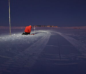 Expeditioner kneeling on the sea ice in semi-darkness installing a gauge