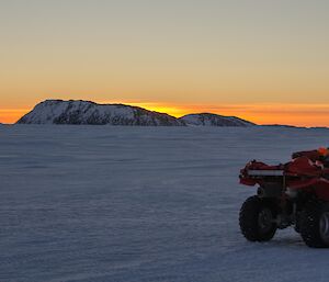 Quad bike on the sea ice with a bright and colourful sunset in the background